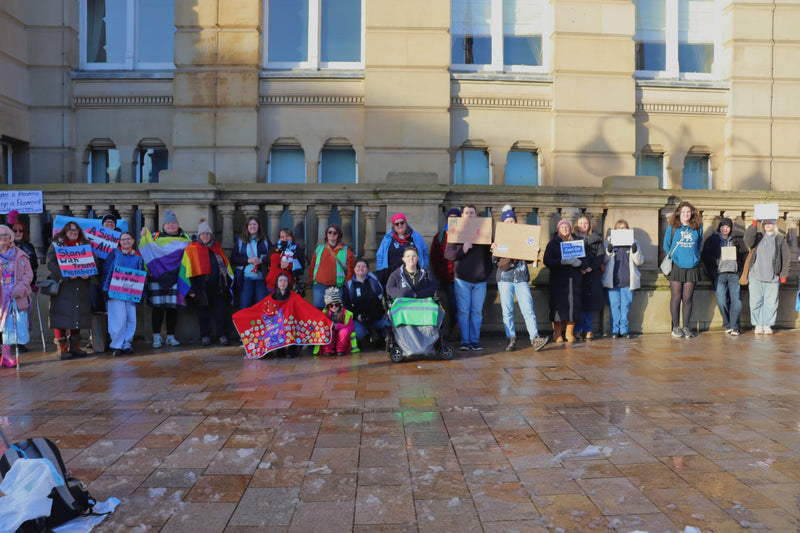 About 30 protesters against a wall holding up signs