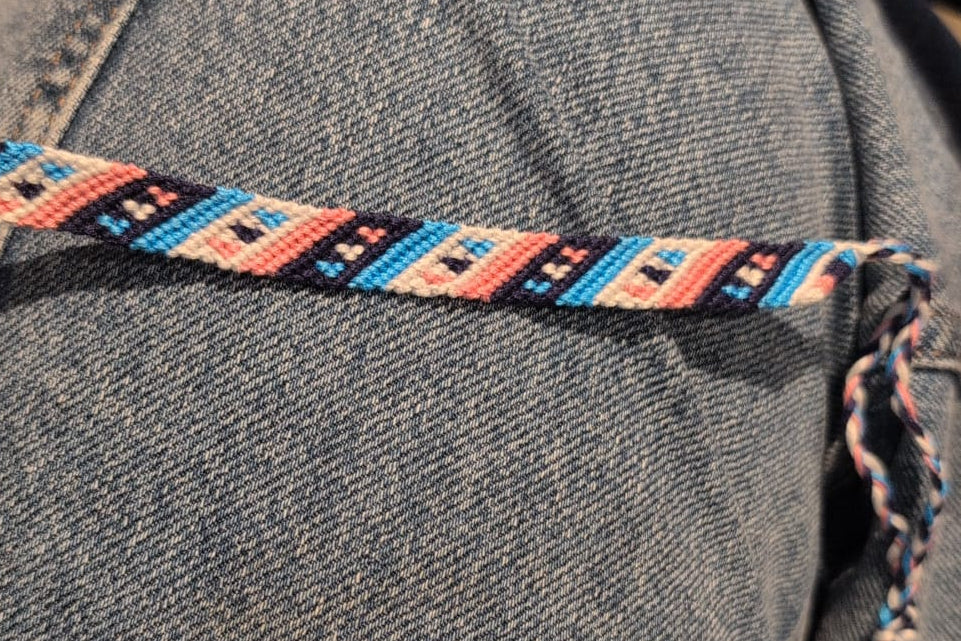 A woven friendship bracelet made out of pink, blue, white and navy thread to form a diagonal pattern with hearts.